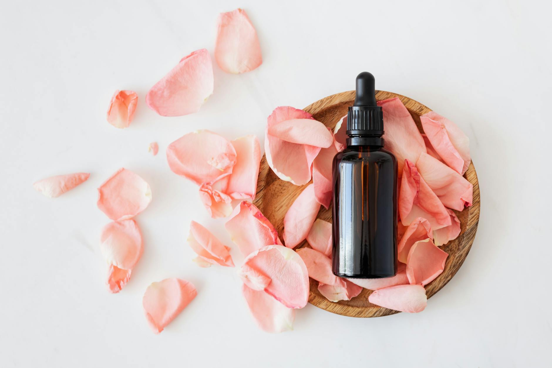 composition of cosmetic bottle with pink rose petals and wooden plate ; launch your product